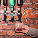 Hand houdt een glas rode drank vast onder een drankdispenser met groene en rode vloeistoffen.