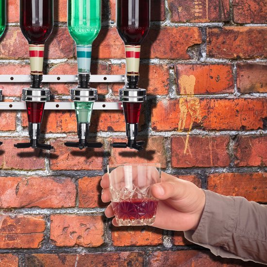 Hand houdt een glas rode drank vast onder een drankdispenser met groene en rode vloeistoffen.