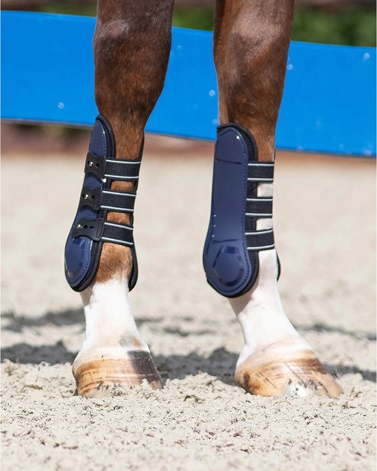 Paardenbenen met donkerblauwe peesbeschermers en witte bandjes, op zand.