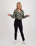Model met zwarte slim fit broek en zwart-groene blouse met grafische print.
