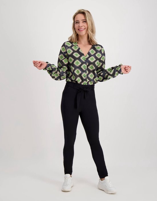 Model met zwarte slim fit broek en zwart-groene blouse met grafische print.