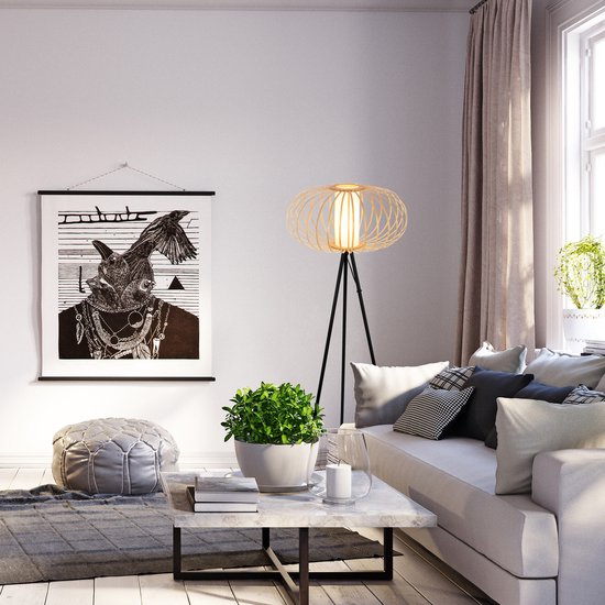 Staande lamp met open bamboe lampenkap en zwart statief in een woonkamer bij een raam.