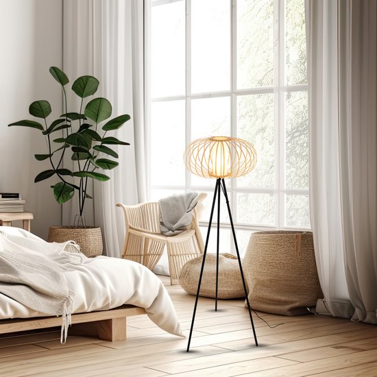 Een staande lamp met open bamboe lampenkap en zwart statief in een slaapkamerinterieur bij een raam.