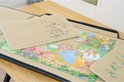 Een geopende puzzelmap met een legpuzzel van kabouters en tractoren. Twee rode bakjes met stukjes liggen ernaast.