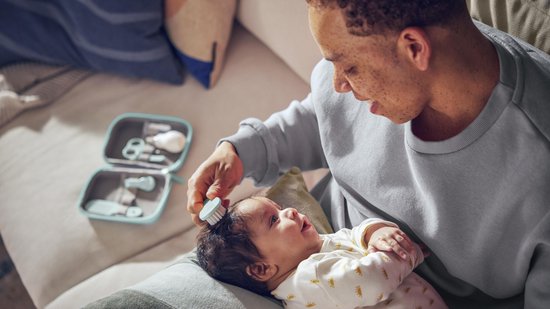Baby wordt gekamd door vader met een mintgroene borstel uit de babyverzorgingsset, de set ligt ernaast.