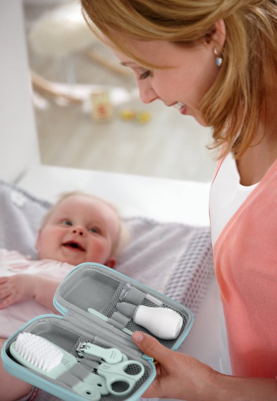 Moeder houdt een open mintgroene babyverzorgingsset vast met verzorgingsproducten voor een baby die lacht.