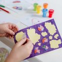 Een kind trekt een gele sticker van een vel met Peppa Pig afbeeldingen.