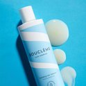 Lichtblauwe fles met witte golvende strepen. Drie druppels product liggen ernaast op een blauwe achtergrond.