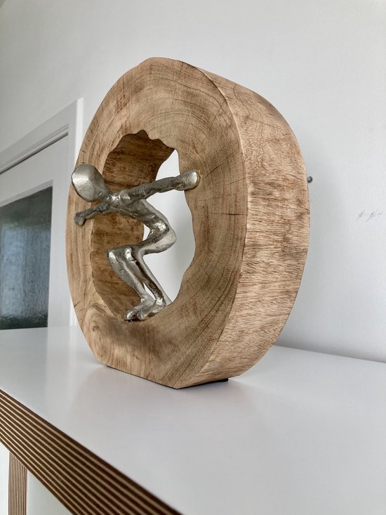 Figurine argentée se faufilant à travers un disque en bois, placée sur une étagère blanche.