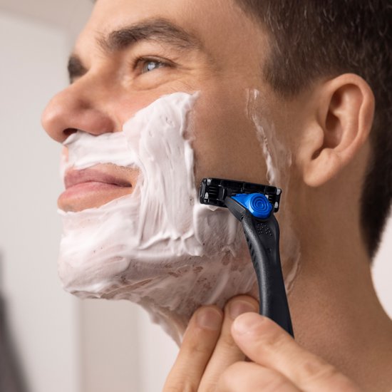Homme avec mousse à raser sur le visage utilisant un rasoir BIC Hybrid 3 Flex, noir avec des détails bleus.