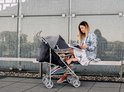 Vrouw in spijkerjasje leest bij een grijze buggy met kind.