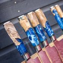 Close-up van zes messengrepen met blauw epoxy en hout, in een houten messenblok.