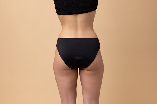 Arrière d'une femme portant un bas de bikini noir taille basse sur fond beige.
