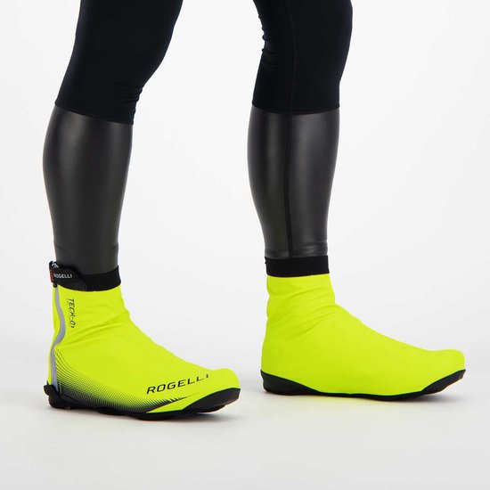 Close-up van benen in zwarte fietskleding met fluor gele Rogelli Tech-01 overschoenen.