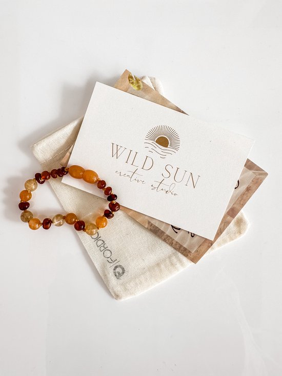 Barnstenen armband met oranje en gele kralen, liggend op een stoffen zakje naast een kaart met het 'Wild Sun creative studio' logo.