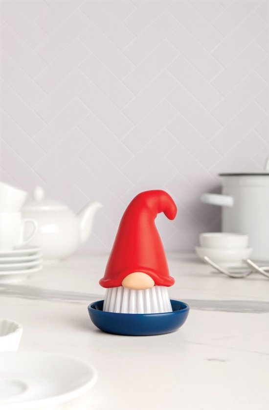 Een afwasborstel in de vorm van een gnome met een rode puntmuts, beige neus en witte borstelharen, staand in een donkerblauwe houder.