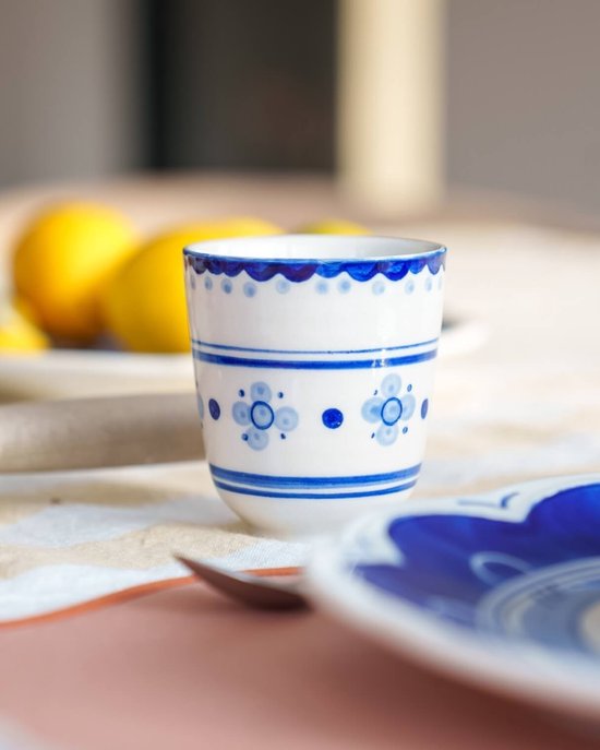 Wit porseleinen bekertje versierd met blauwe golven en bloemmotieven op een tafel met citroenen.