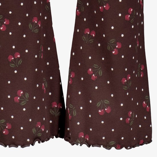 Detailopname van roodbruine ribbroek met kersenprint, witte stippen en een gegolfde zoom onderaan de pijpen.