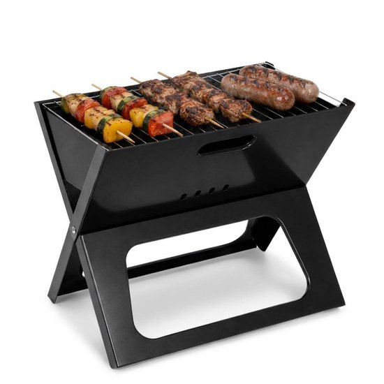 Zwarte inklapbare barbecue met vleesspiesen, worstjes en groentespiesen.