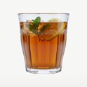 Un verre Duralex Picardie transparent avec cannelures verticales, rempli de thé glacé, citron et menthe.