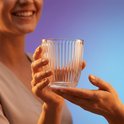 Une femme souriante tient un verre côtelé, offert par une autre personne.