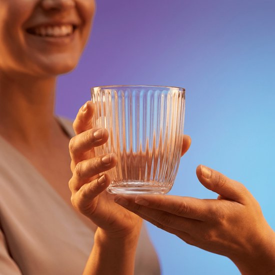 Une femme souriante tient un verre côtelé, offert par une autre personne.