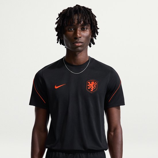 Model draagt een zwart sportshirt met oranje Nike logo op de borst en Nederlands elftal logo.