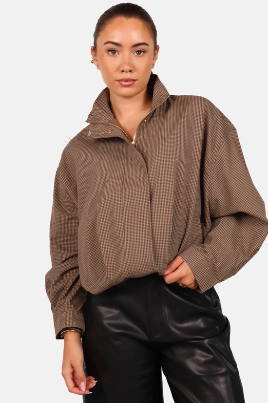 Model in close-up met bruin bomberjack met ruiten, ritssluiting en zwarte leren broek.