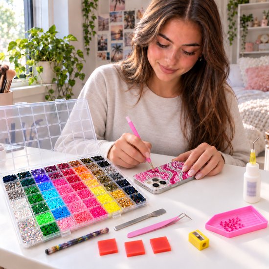 Vrouw versiert een telefoonhoesje met roze strass steentjes uit een uitgebreide sorteerdoos met 60 verschillende kleuren.