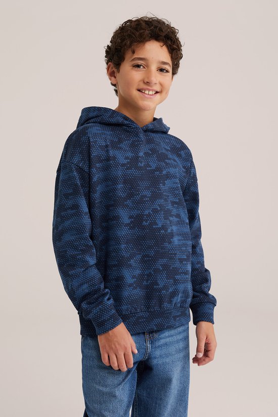 Glimlachende jongen in een marineblauwe hoodie met een zeshoekig patroon, gezien vanaf de taille omhoog.