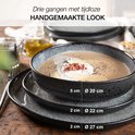 Grijze aardewerken soepkom met room, bovenop een dinerbord en een plat bord met afmetingen.