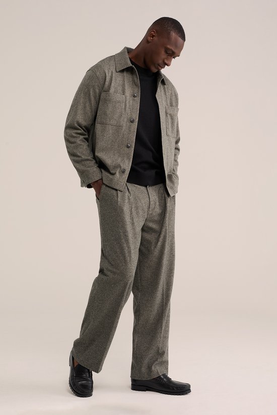 Man in zwart coltrui, grijze broek en jasje met borstzakken.
