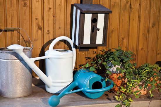 Tuinspullen: twee gieters (wit en zilver), een blauwe gieter, potten met planten en een zwart-wit gestreept vogelhuisje.