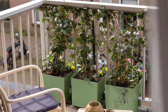 Drie olijfgroene Vercony plantenbakken met klimop en bloemen, bevestigd aan een balkonhek bij een zithoek.