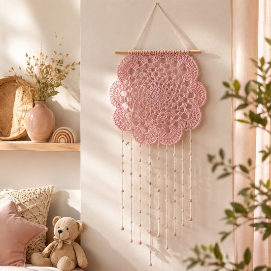 Roze gehaakte dromenvanger in bloemvorm met kralen aan touwtjes, hangend aan een houten stok.