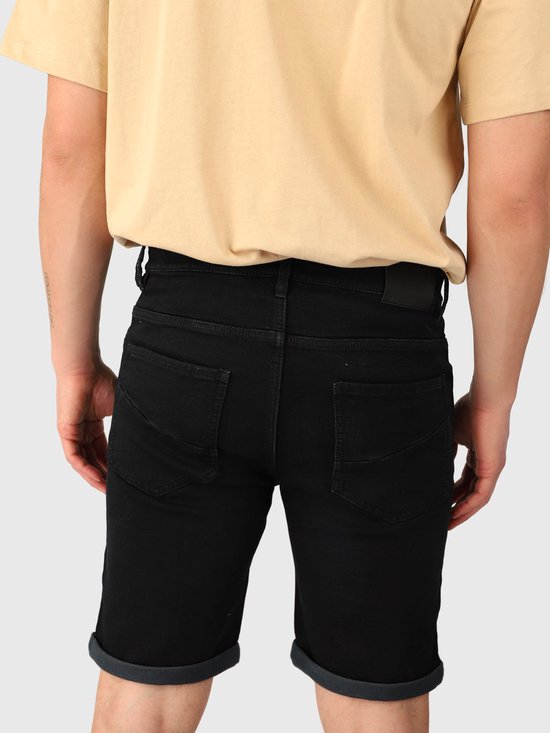 Achterkant van een model in zwarte denim shorts met opgerolde zomen en een beige T-shirt.