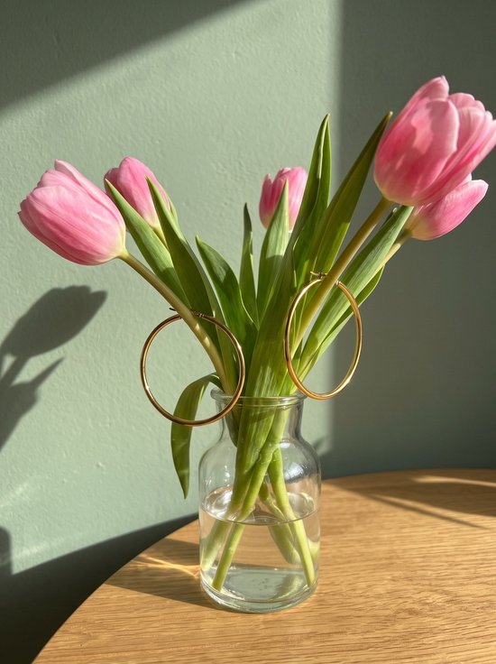 Goudkleurige hoepeloorbellen hangend aan de stelen van een boeket roze tulpen in een glazen vaas.