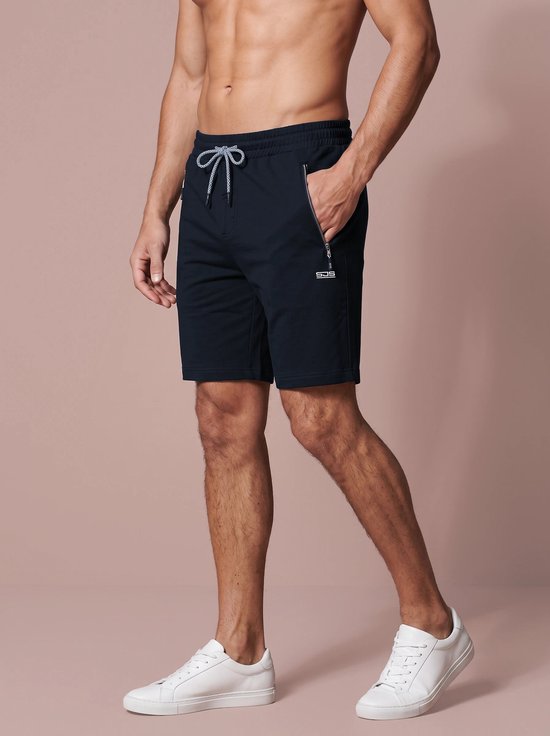 Model draagt marineblauwe sportshort met ritszakken, wit trekkoord en wit SJS-logo op de dij.
