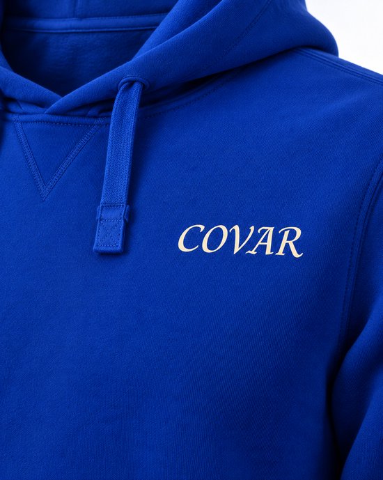 Detailopname van koningblauwe hoodie met witte 'COVAR' tekst op de borst en trekkoord.