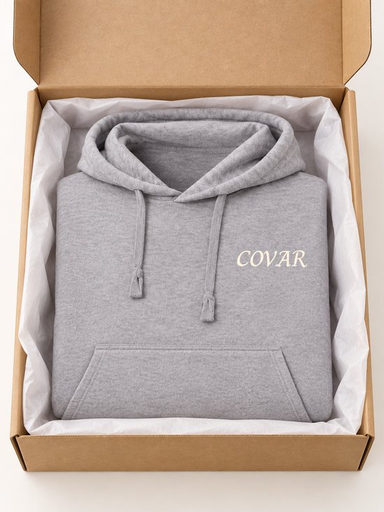 Grijze hoodie met 'COVAR' print op linkerborst, in open kartonnen doos.