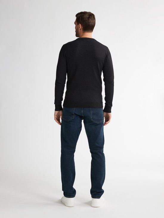 Model op de rug gezien, draagt een zwarte fijngebreide trui, donkerblauwe jeans en witte sneakers.