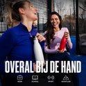 Twee lachende vrouwen op een sportveld, één met een witte fles, de ander met een rode fles. "OVERAL BIJ DE HAND"