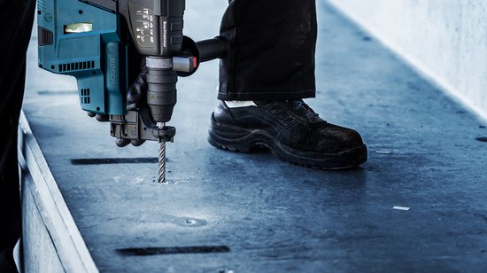 Detailopname van een Bosch boorhamer die een gat boort in een betonnen ondergrond.