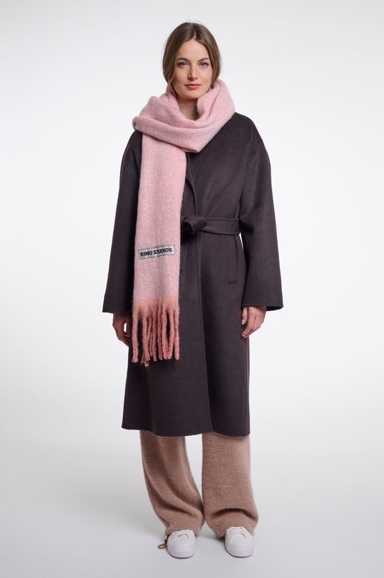 Model in een donkergrijze mantel en beige broek met een roze, gefranjde sjaal voorzien van het RINO STUDIOS-label.