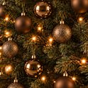Close-up van een kerstboom met bruine ballen in drie texturen, verlicht door warme kerstlampjes.