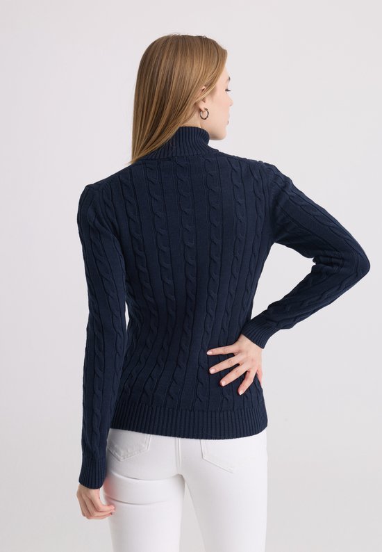 Achterkant van een donkerblauwe kabeltrui met ritskraag, gedragen door een model met witte broek.