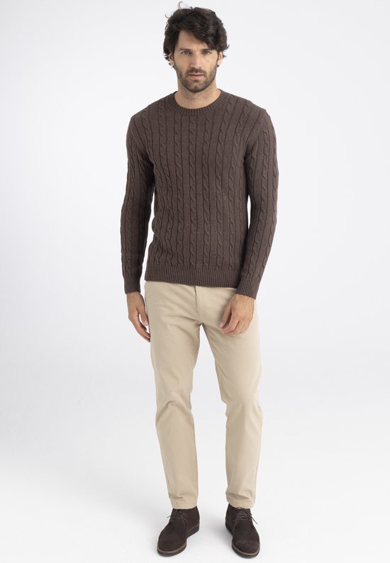 Man met bruine kabeltrui en beige broek, staand.
