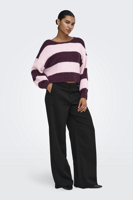 Een model draagt een trui met horizontale strepen in roze en bordeauxrood, met een zwarte broek.