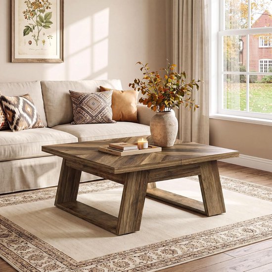 Vierkante salontafel met houten blad in visgraatpatroon, U-vormige poten, bij een beige bank met decoratieve kussens en een vaas met herfsttakken.