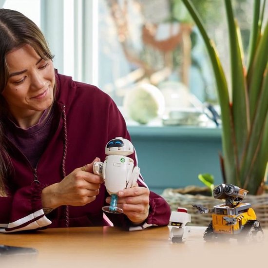 Femme tenant une EVE LEGO avec une tige bleue, à côté de WALL-E LEGO et d'un petit robot blanc.